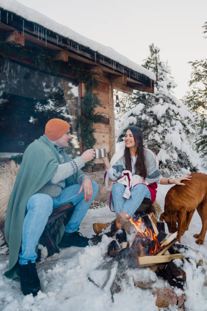istock Couple with dog siting around fire pit in front of the cabin 2189827258