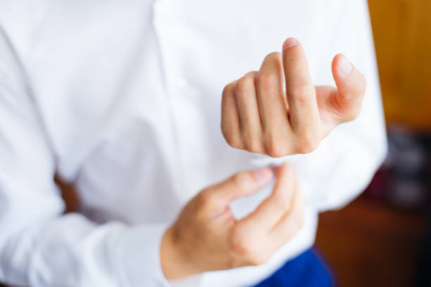 the groom in a white shirt buttoning a button on cuff.