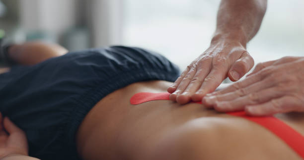 Physiotherapist, hands and tape for back pain with recovery process for injury, help and bed at clinic. People, biokinetics and treatment for rehabilitation with muscle, spine and service at hospital fisioterapeuta, manos y cinta para el dolor de espalda con proceso de recuperación de la lesión, ayuda y cama en la clínica. personas, biocinética y tratamiento para la rehabilitación con músculo, columna vertebral y servicio hospitalario