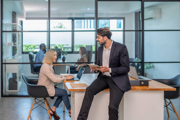 istock portrait business man casual using digital tablet and talking with colleague while sitting on desk in the room,multiracial business people working in the office 2189866936