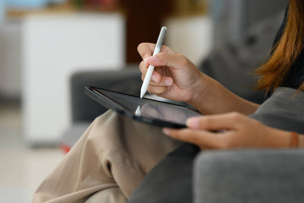 istock Close up woman using a stylus pen to write or draw on blank tablet screen, relaxing on couch 2189877012