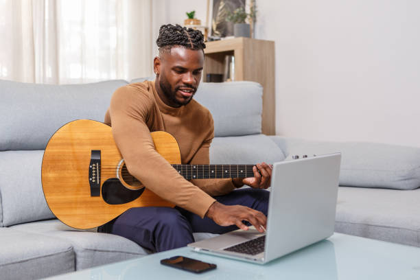 istock Man takes online guitar lessons while sitting on a couch at home during the day 2189901016