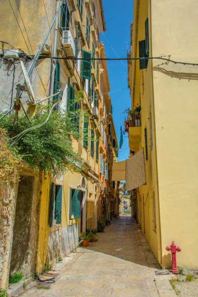 A quiet residential road in the historic centre of Corfu Old Town, Greece, including the house of inc house of painter Spiridione Scarvelli on left who once lived there. A UNESCO World Heritage Site, it is a stunning blend of Venetian, French and British architectural influences. The Old Town features narrow, winding alleys of pastel-coloured Venetian buildings