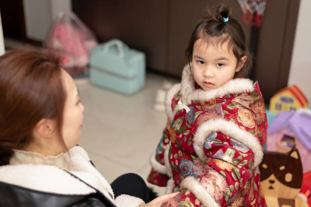 The young Chinese  mother dresses her daughter for the celebration party . Her daughter is wearing traditional Chinese clothes. They're getting ready for celebrating  Chinese New Year.