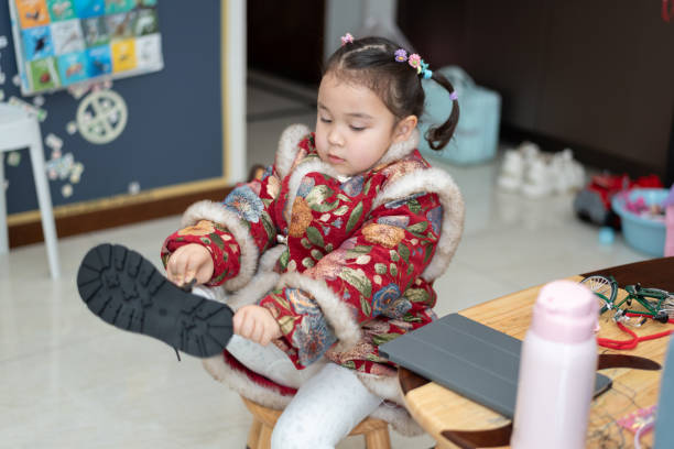 A little Chinese girl is getting ready for the Chinese New Year celebration, her mother combed her hair and put on a traditional Chinese New Year costume. She is now putting on her boots to be ready for the celebration