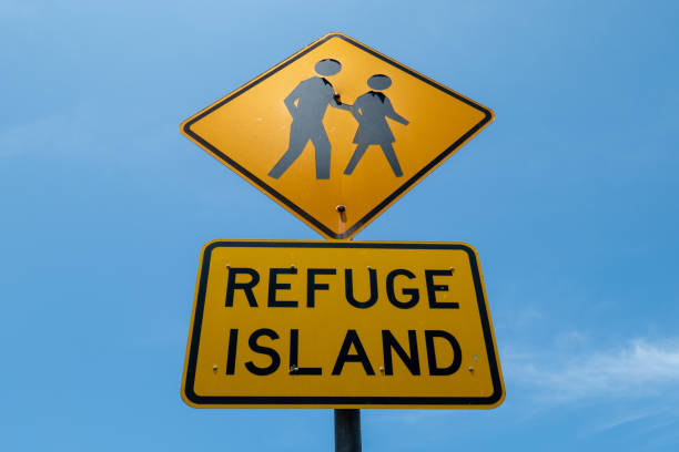 A Refuge Island road sign on Sydney Road, Manly, warning motorists of an island in the middle of the road to help pedestrians cross the road.  This image was taken on a hot and sunny afternoon on 13 December 2024.
