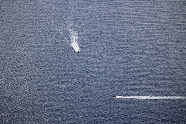 Two speedboats leaving white trails on the vast blue ocean, creating a dynamic and minimalistic marine scene .