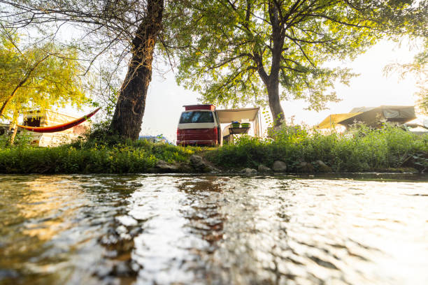 Van Is Parked by the Riverside,Set Up for a Peaceful Camping Getaway. The Serene Location Offers a Perfect Spot for Outdoor Adventure and Relaxation.