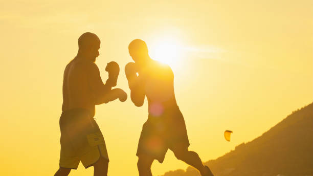 Martial Artists Engage in a Dynamic Training Session on the Beach,Silhouetted Against the Warm Hues of Sunset. The Scene Captures the Intensity of their Practice Blended with the Serene Beauty of the Evening Shoreline Title