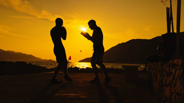 Two Martial Artists Engage in a Sparring Session on the Beach During Sunset. The Warm Golden Light of the Setting Sun Highlights their Focused Movements,Capturing the Energy and Discipline of their Training