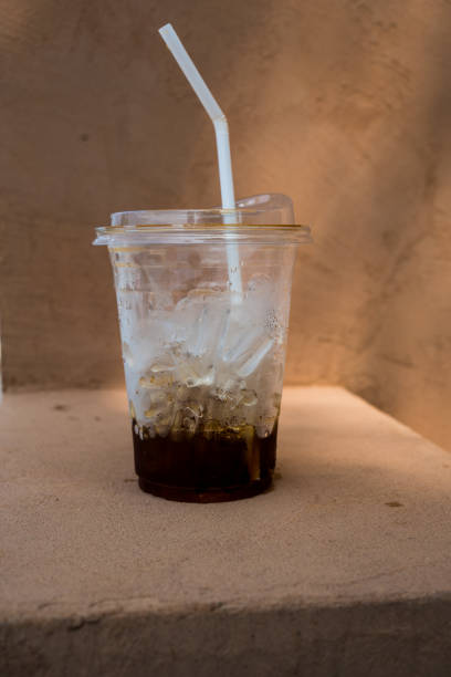 Close up of iced coffee plastic cup with a little coffee left on the bottom in the orange block background.