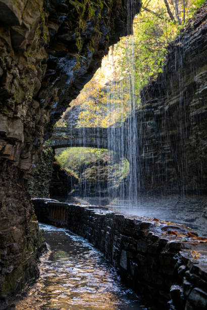 istock Water cascades down rocky cliffs in a tranquil Watkins Glen State Park surrounded by autumn foliage near a stone bridge, highlighting nature's beauty in a secluded area 2189938306