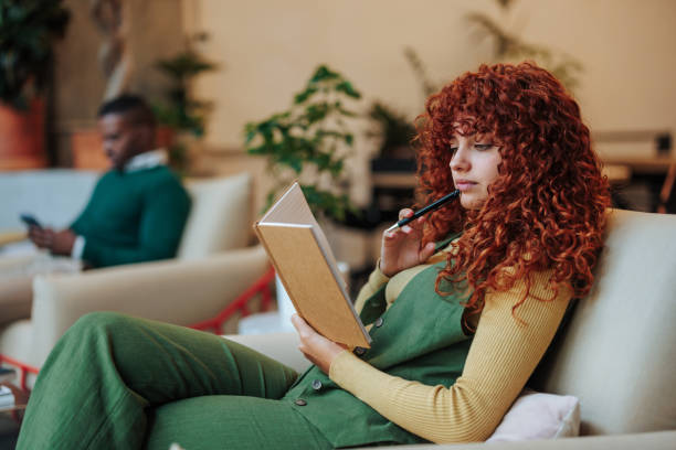 Redhead businesswoman reading notes on notebook and thinking about new business strategies in a modern co-working office