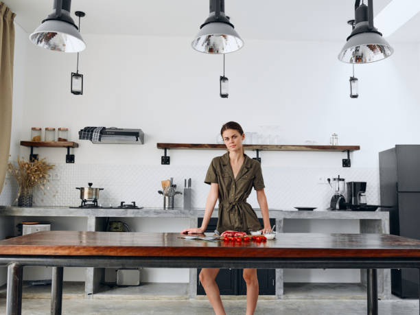 istock Happy woman standing full-length in Stylish minimalist kitchen interior with natural elements in wood and stone design with fresh produce for dinner on the table 2189946632
