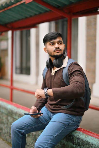istock Young man sitting at a bus stop and checking the time 2189947048
