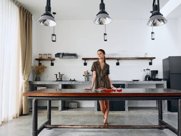 istock Happy woman standing full-length in Stylish minimalist kitchen interior with natural elements in wood and stone design with fresh produce for dinner on the table, copy space 2189948050