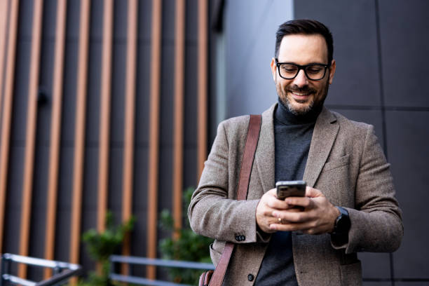 istock Smiling businessman using mobile phone outside office building 2189953111