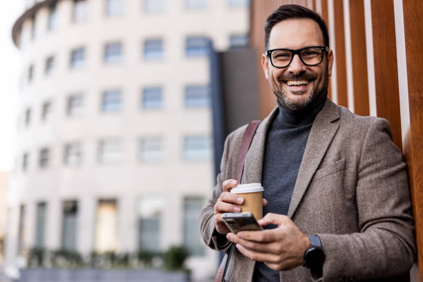 istock Smiling businessman using smartphone and drinking coffee outdoors 2189953140