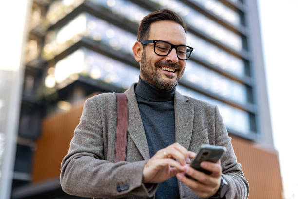 istock Smiling businessman using smartphone in front of modern office building 2189953153