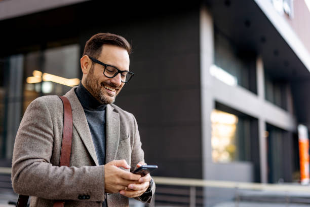 istock Smiling businessman using smartphone in front of office building 2189953165