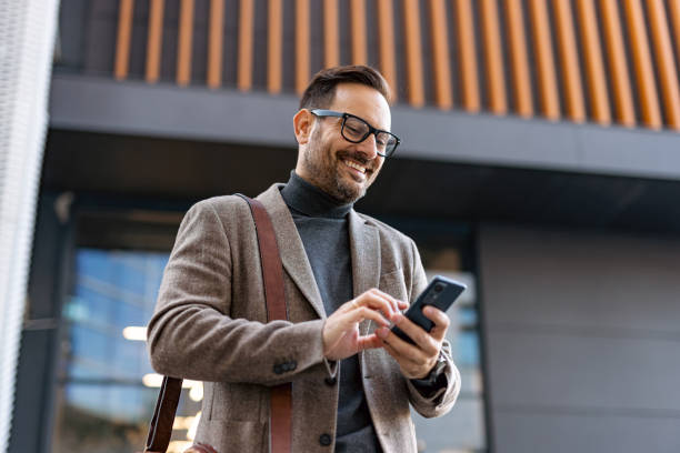 istock Smiling businessman using smartphone in front of office building 2189953173