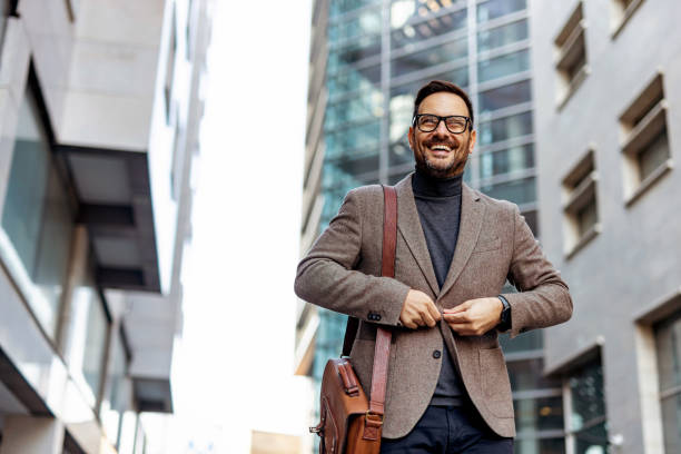 istock Smiling businessman buttoning his jacket while walking in the city 2189953174