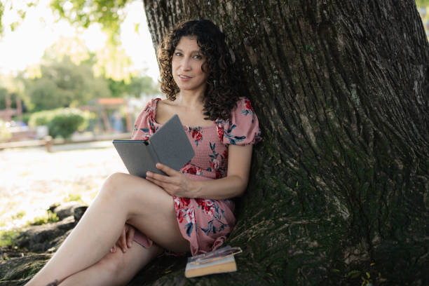 istock Woman reading an ebook under a tree in a park 2189956979