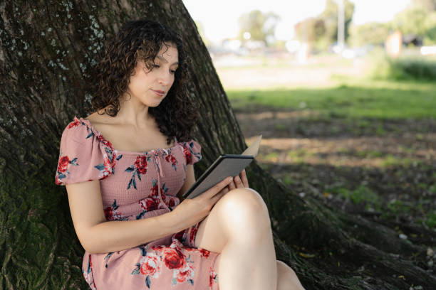 istock Young woman reading an e-reader in the park 2189957100