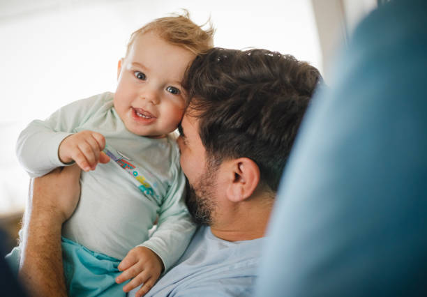 Cheerful father is holding his baby boy at home.