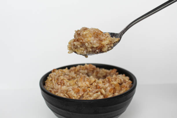 istock Cooked plain rolled oat inside black bowl and one silver spoon, Isolated on white background 2189999363