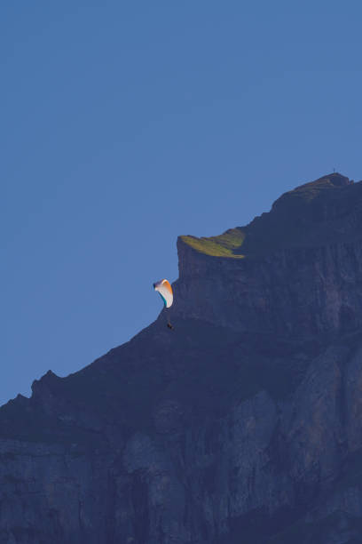 Paraglider in action against a rugged mountain cliff. Adventure seeker flying high. Scenic landscape perfect for outdoor sports enthusiasts and nature lovers.K