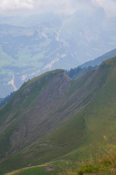 Scenic view of a green mountain ridge under a cloudy sky. Rolling hills and distant valleys create a majestic alpine panorama.K