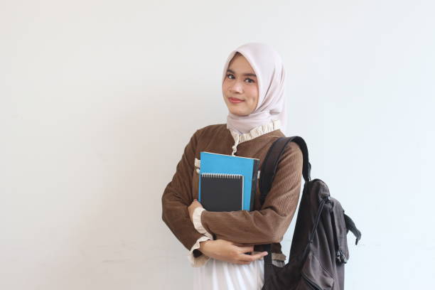 istock Smiling Muslim Student Girl Holding Notebooks and Backpack Against White Wall, Ready for Education 2190004062