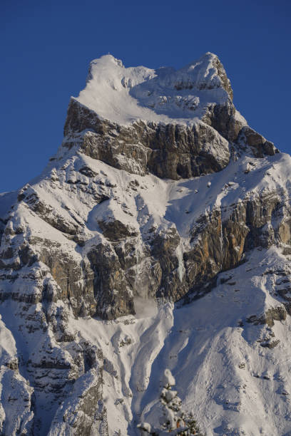 Majestic snow-capped peak under a bright blue sky. Rugged cliffs with fresh snow. Perfect for winter landscapes or alpine exploration themes.