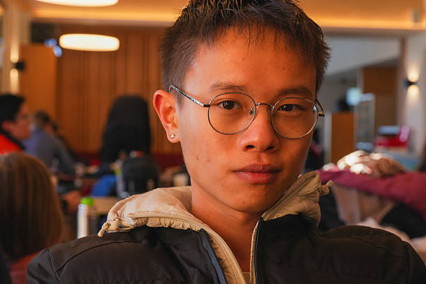 Focused young individual sitting in a warmly lit cafe, wearing casual attire. The setting is bustling with activity. Calm atmosphere in a modern coffee shop.