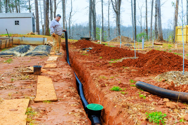 istock Man installing drainage system in backyard garden area surrounded by trees during overcast day 2190009049
