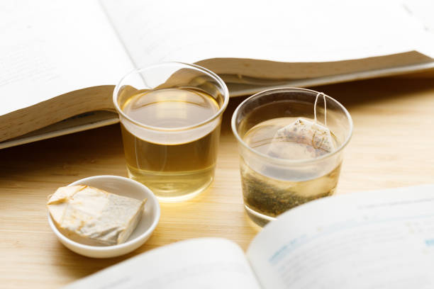 Cup of hot tea with tea bag and text book on wooden table. Study time. selective focus.