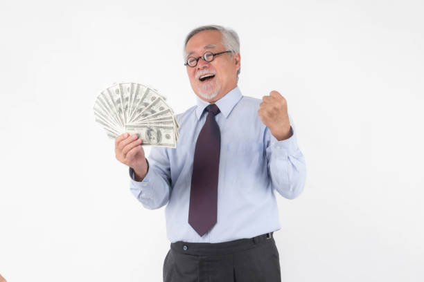 istock Senior Asian businessman celebrating financial success while holding a large stack of US dollar banknotes with a cheerful and excited expression, wearing formal attire , isolated on white background 2190014927