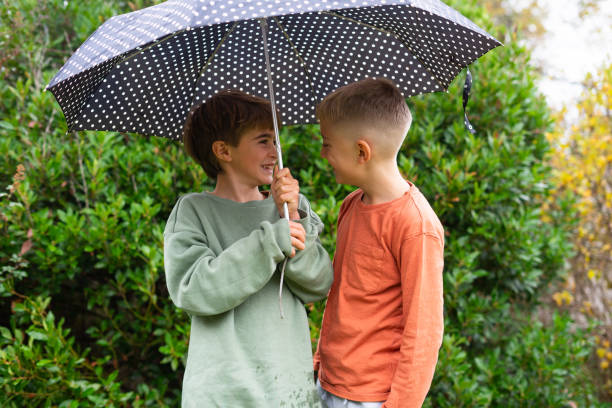 istock Two boys sharing umbrella, smiling and having fun outdoors 2190022551