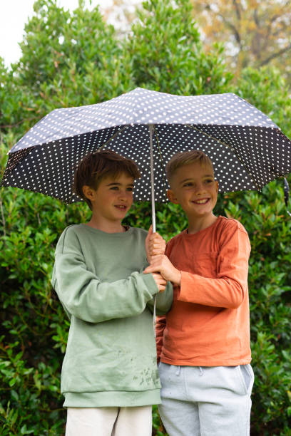 istock Two smiling boys holding a polka dot umbrella in a garden 2190022637