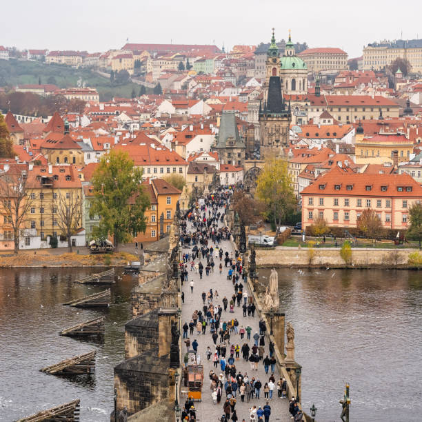 A moody, rainy autumn morning in Prague, with the historic Old Town buildings and the iconic Old Town Bridge Tower. The 14th-century Charles Bridge spans the Vltava River, a central symbol of the city that connects key districts and reflects Prague's rich medieval and architectural heritage.