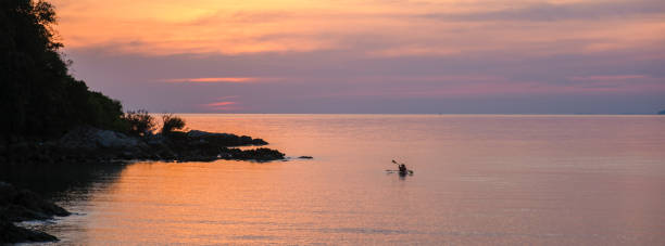 Soft hues of orange and purple paint the sky as a lone kayaker glides across the calm waters of Koh Munnork Island. A serene and breathtaking moment at dusk awaits all who visit Thailand.