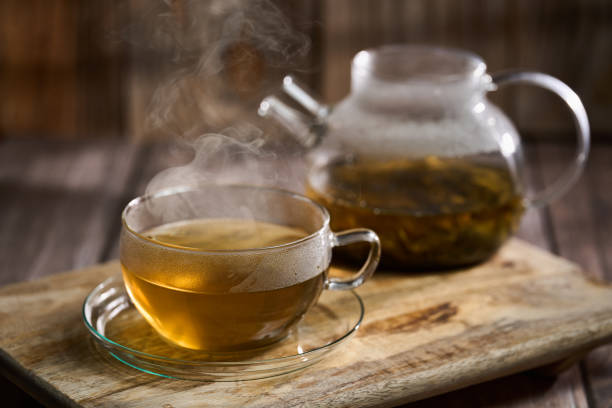 Cinematic shot of a hot Japanese Sencha tea in a large glass cup with a glass teapot on a rustic wooden board