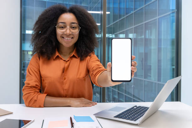 istock Smiling woman in office holding smartphone with blank screen for advertisement 2190036038