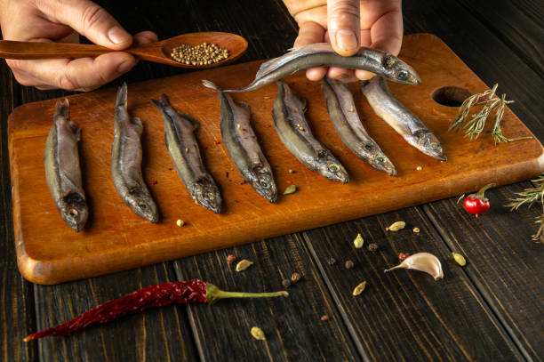 istock A hand skillfully holds a fish while arranging freshly caught specimens on a rustic wooden board. Surrounding spices and herbs add a touch of flavor and artistry to the culinary display. 2190037312