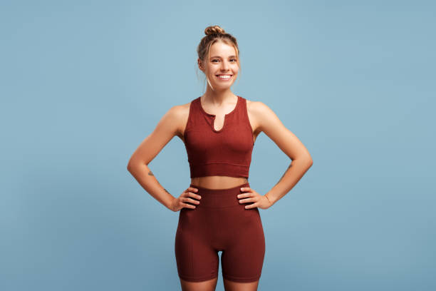 istock Smiling sporty woman holding hands on hips over blue background in studio 2190040497