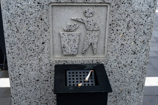 A sign shows a person disposing waste properly into a trash bin in a busy urban setting, promoting cleanliness and responsibility