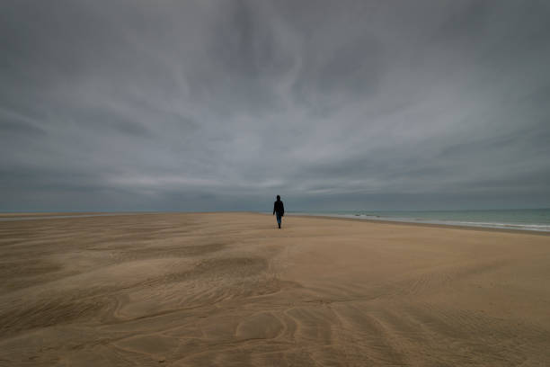 istock person walking along a deserted beach, dramatic sky 2190054258