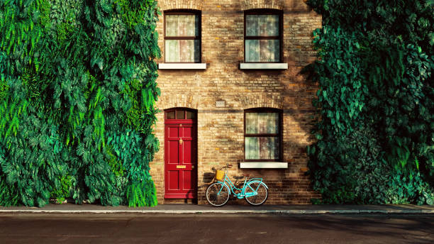 Beautiful brick building with a bold red door at the center, framed by lush green foliage on both sides. Above the door, two windows with curtains add symmetry. A vintage turquoise bicycle with a basket leans against the wall, adding a pop of color and charm to the peaceful urban setting. The vibrant greenery contrasts elegantly with the warm brickwork, creating a harmonious balance between nature and architecture.