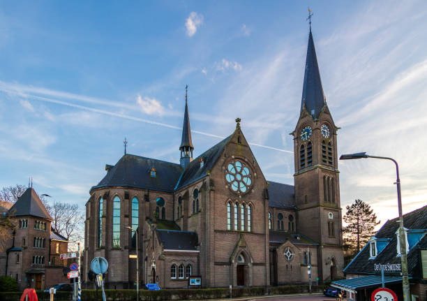 The prominent St. Andreas Church and its clock tower dominate the Katwijk aan Zee cityscape under a clear blue sky, with a street and buildings in the foreground.